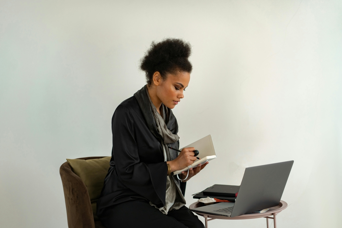 woman writing in a journal with laptop